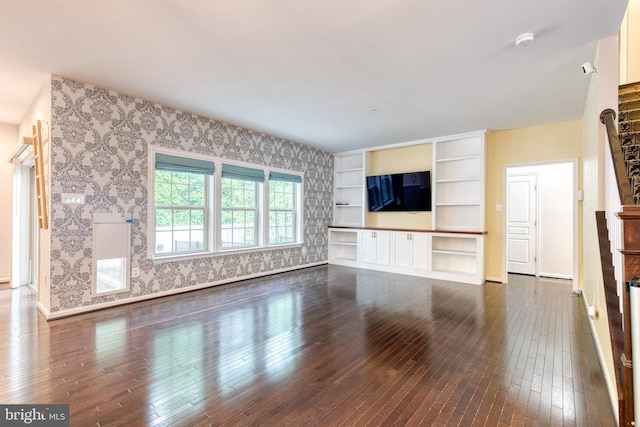 unfurnished living room featuring dark wood-style flooring, wallpapered walls, and baseboards