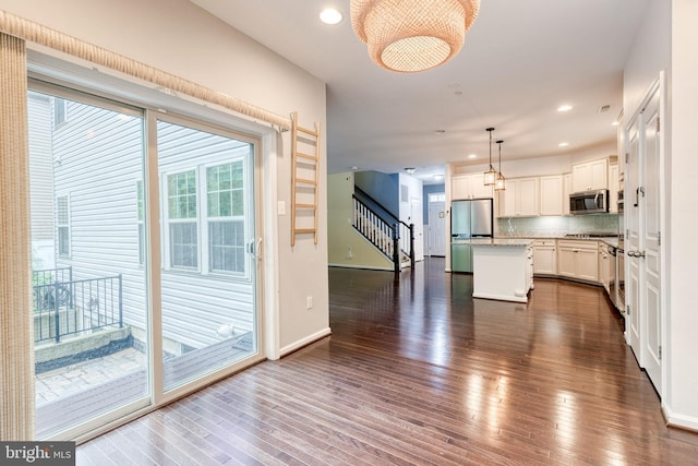 kitchen featuring appliances with stainless steel finishes, a center island, dark wood-type flooring, hanging light fixtures, and decorative backsplash