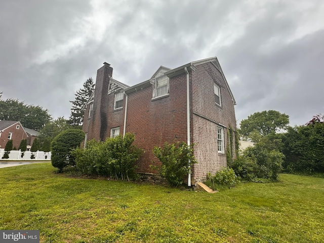 view of side of home featuring brick siding, a chimney, and a yard