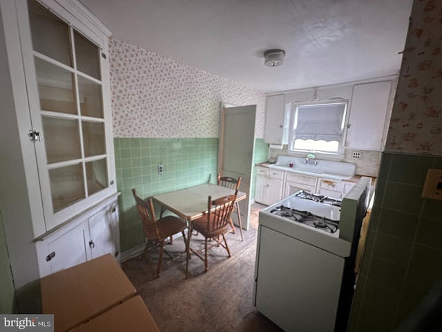 kitchen with wallpapered walls, white range with gas stovetop, tile walls, wainscoting, and a sink