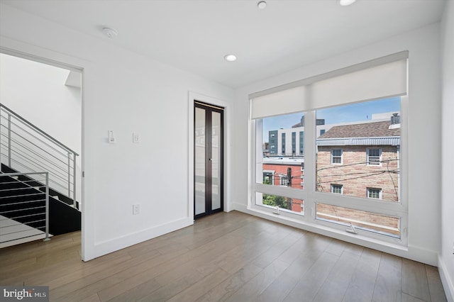 empty room with stairway, wood finished floors, baseboards, recessed lighting, and a smoke detector