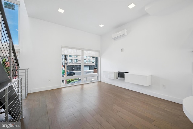 unfurnished living room featuring a wall unit AC, wood finished floors, and baseboards