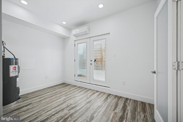 unfurnished room featuring electric water heater, a wall unit AC, wood finished floors, french doors, and baseboards