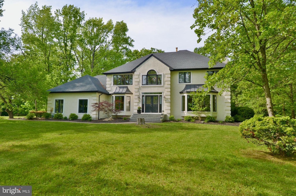 view of front of house with stucco siding, a front yard, and a shingled roof