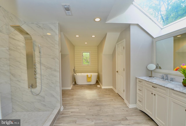 bathroom with a skylight, vanity, a freestanding tub, tiled shower, and recessed lighting