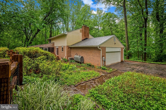 view of side of property with brick siding, a garage, a chimney, asphalt driveway, and central AC
