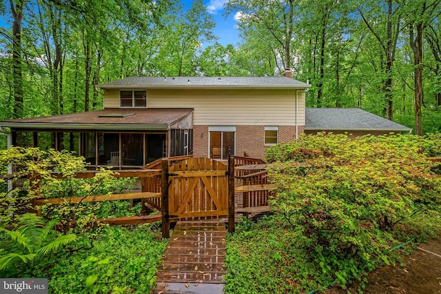 rear view of property with a sunroom, a chimney, brick siding, and roof with shingles