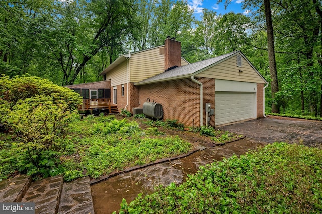 view of property exterior featuring a chimney, a garage, brick siding, heating fuel, and driveway
