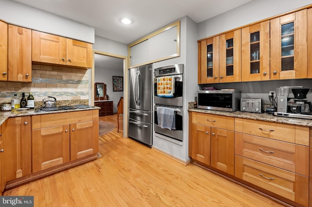 kitchen featuring stainless steel appliances, light wood-style flooring, decorative backsplash, and light stone counters