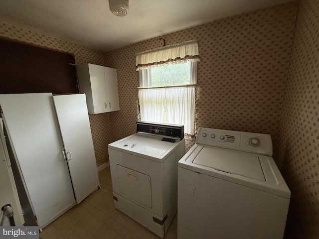 clothes washing area with wallpapered walls, washing machine and dryer, cabinet space, and light flooring