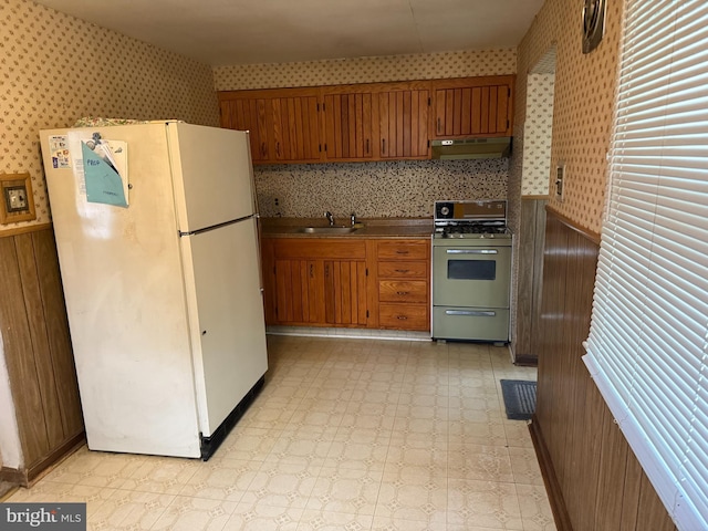 kitchen featuring freestanding refrigerator, gas range, wallpapered walls, under cabinet range hood, and light flooring
