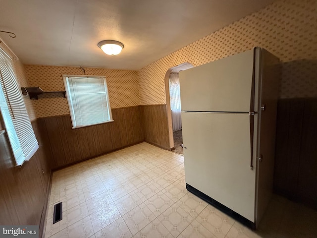 kitchen with freestanding refrigerator, wallpapered walls, a wainscoted wall, wooden walls, and light flooring