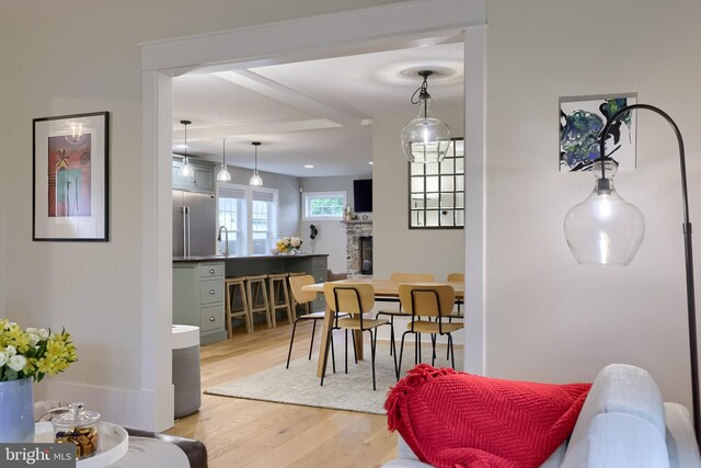 dining area featuring light wood finished floors, a stone fireplace, and beam ceiling