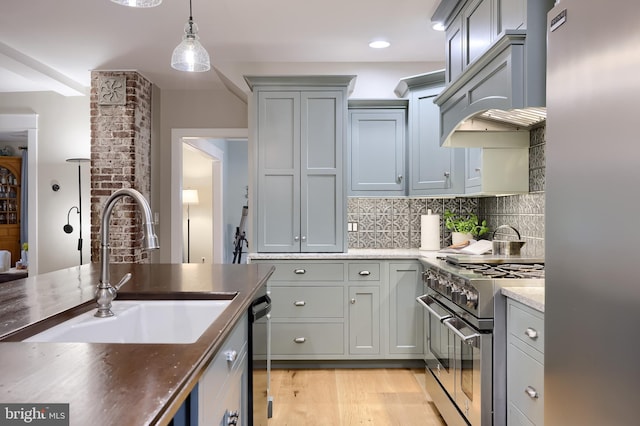 kitchen featuring stainless steel appliances, a sink, custom range hood, light wood finished floors, and backsplash