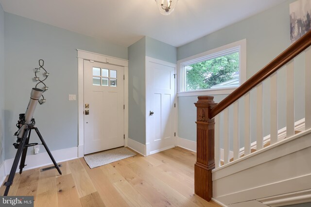 foyer featuring light wood-style flooring, plenty of natural light, stairs, and baseboards