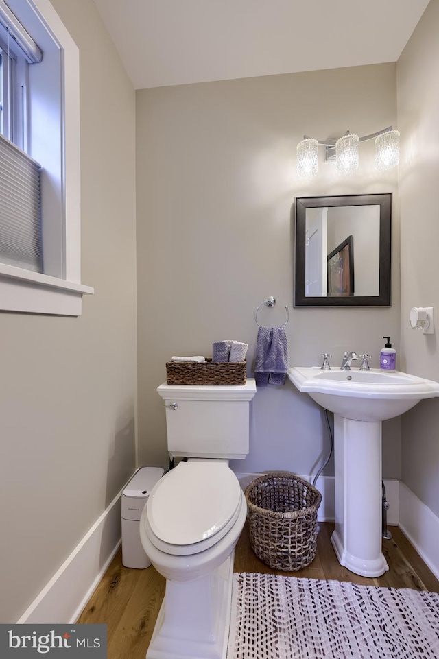 half bathroom with wood finished floors, baseboards, toilet, and a sink