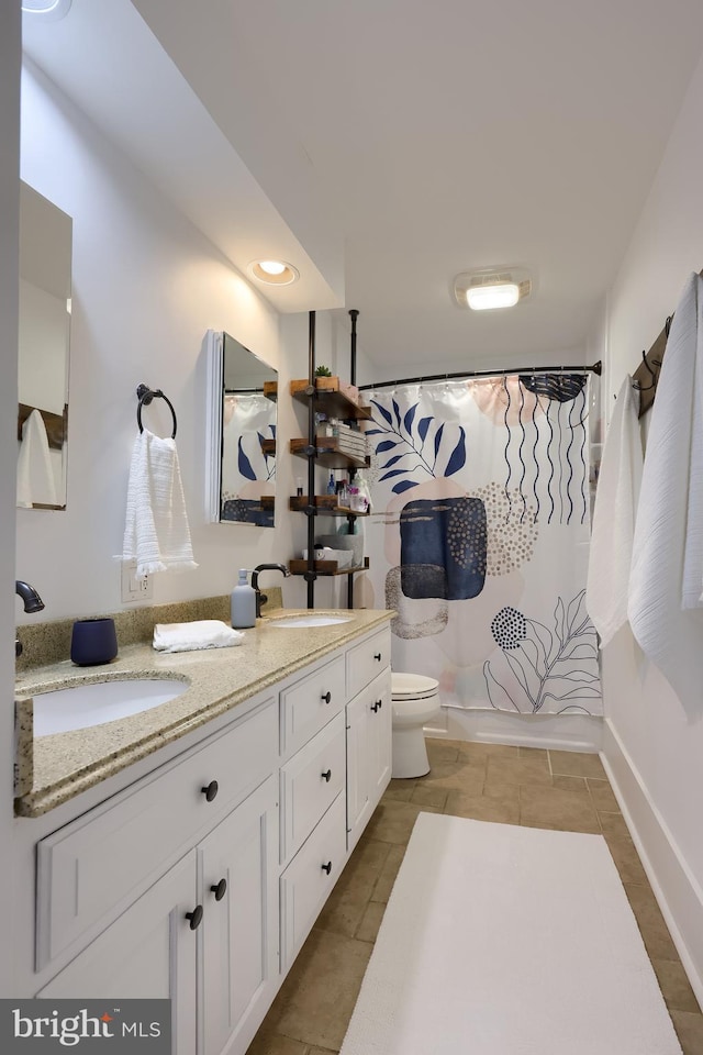 full bath with toilet, a shower with shower curtain, double vanity, tile patterned floors, and baseboards