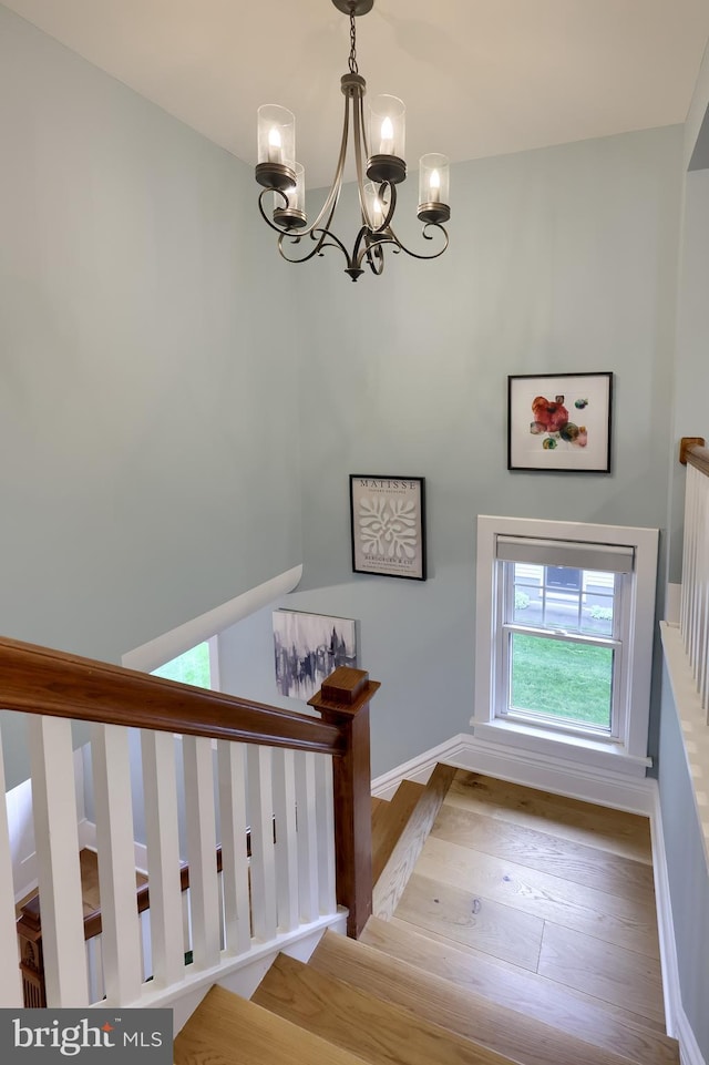 stairway with a chandelier, wood finished floors, and baseboards