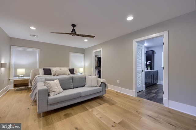 bedroom featuring wood finished floors, baseboards, a walk in closet, ensuite bathroom, and recessed lighting