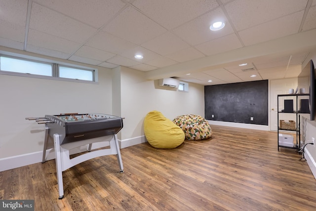 recreation room with wood finished floors, baseboards, a drop ceiling, a wall mounted AC, and recessed lighting