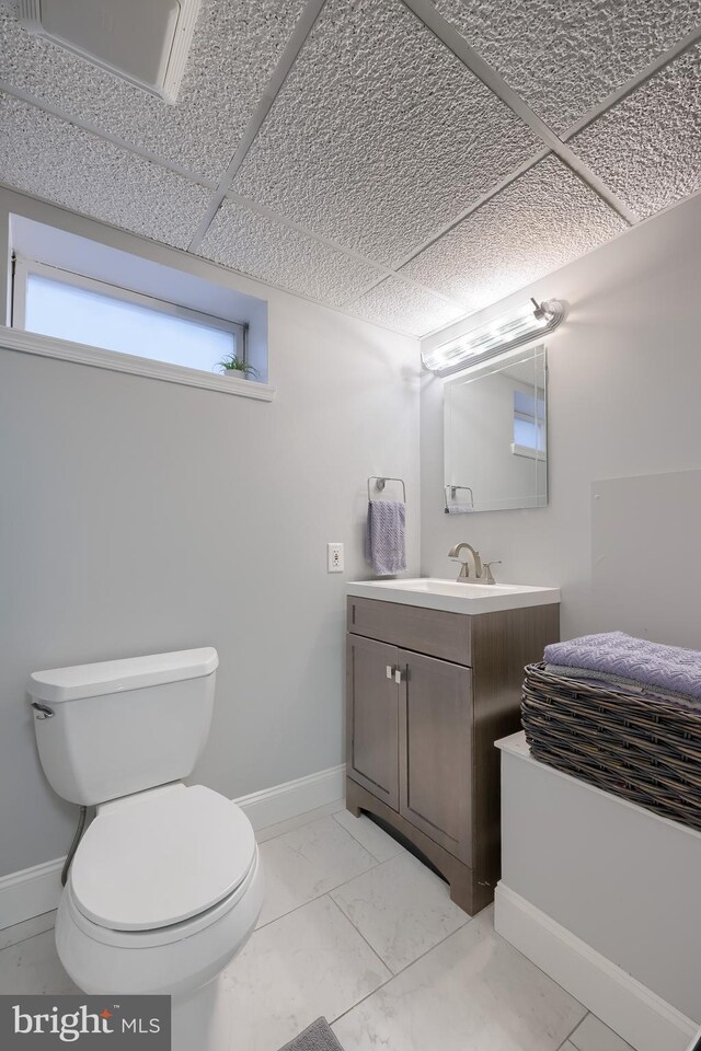 half bathroom featuring toilet, marble look tile flooring, vanity, and baseboards
