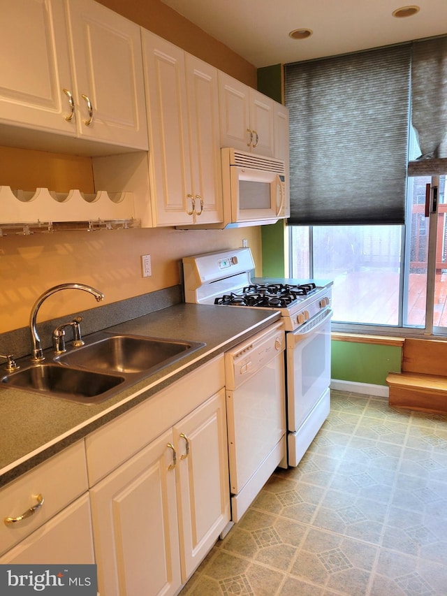 kitchen with white appliances, a sink, white cabinetry, baseboards, and dark countertops