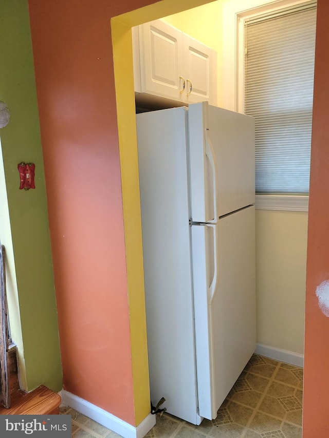 kitchen featuring freestanding refrigerator, white cabinets, and baseboards