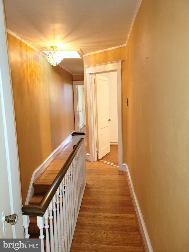 hall with ornamental molding, wood finished floors, a chandelier, and baseboards