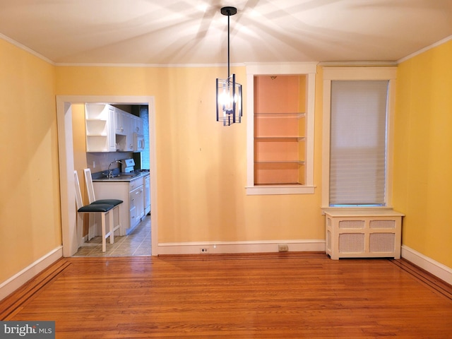 unfurnished dining area with wood finished floors, baseboards, crown molding, built in features, and a sink
