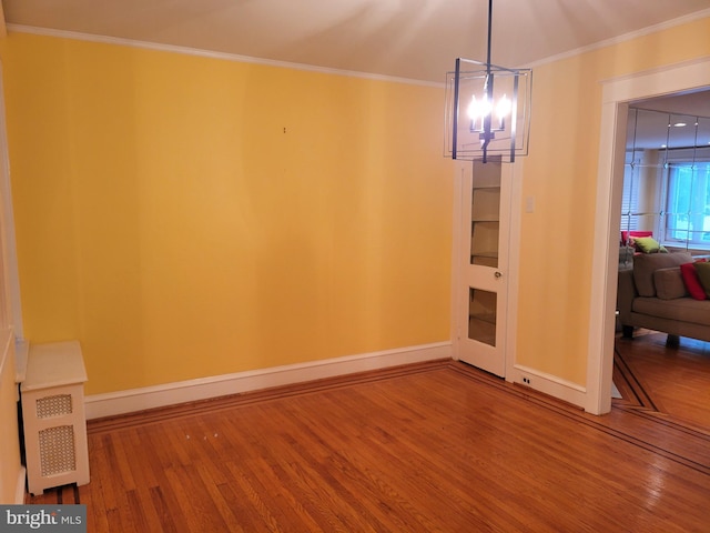 unfurnished dining area with wood finished floors, a chandelier, baseboards, and ornamental molding