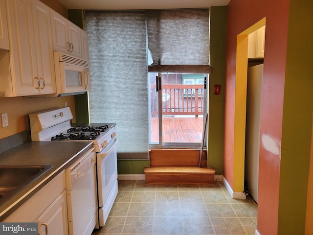 kitchen featuring white appliances, baseboards, dark countertops, and a sink