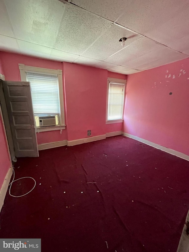 empty room featuring baseboards, a drop ceiling, carpet floors, and cooling unit