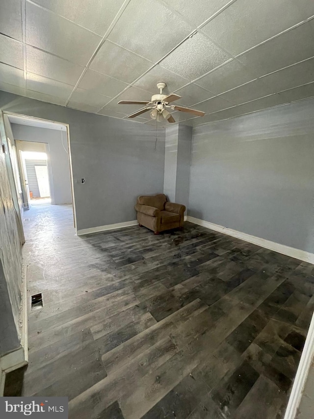 unfurnished room with a ceiling fan, a drop ceiling, baseboards, and wood finished floors