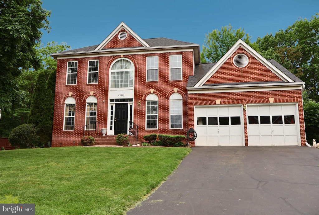 colonial home featuring a garage, brick siding, a front lawn, and driveway
