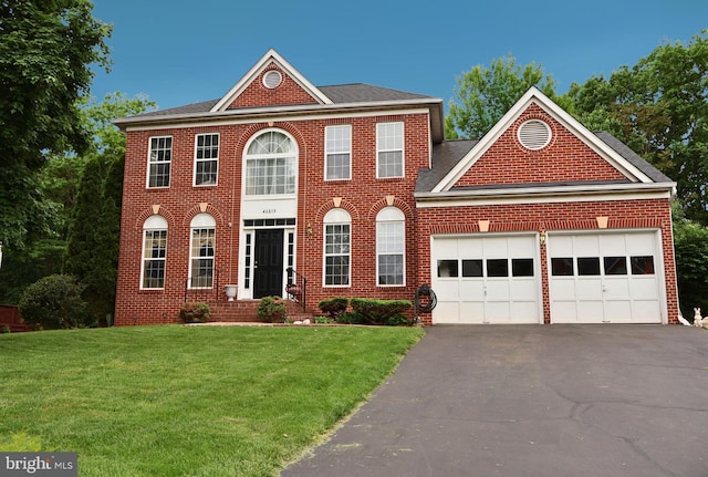 colonial home featuring a garage, brick siding, a front lawn, and driveway
