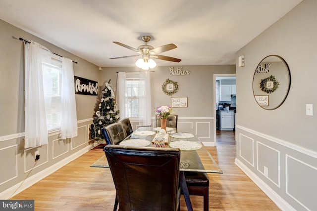dining space featuring a decorative wall, a ceiling fan, a wainscoted wall, and light wood-type flooring