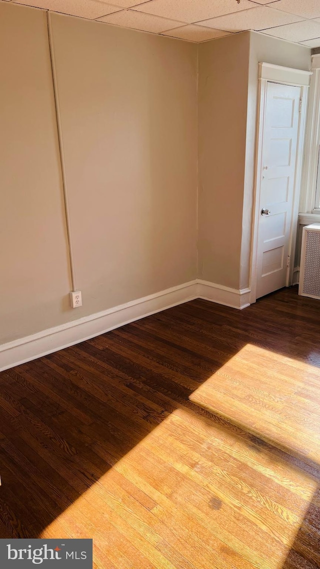 empty room with wood finished floors, baseboards, and radiator heating unit