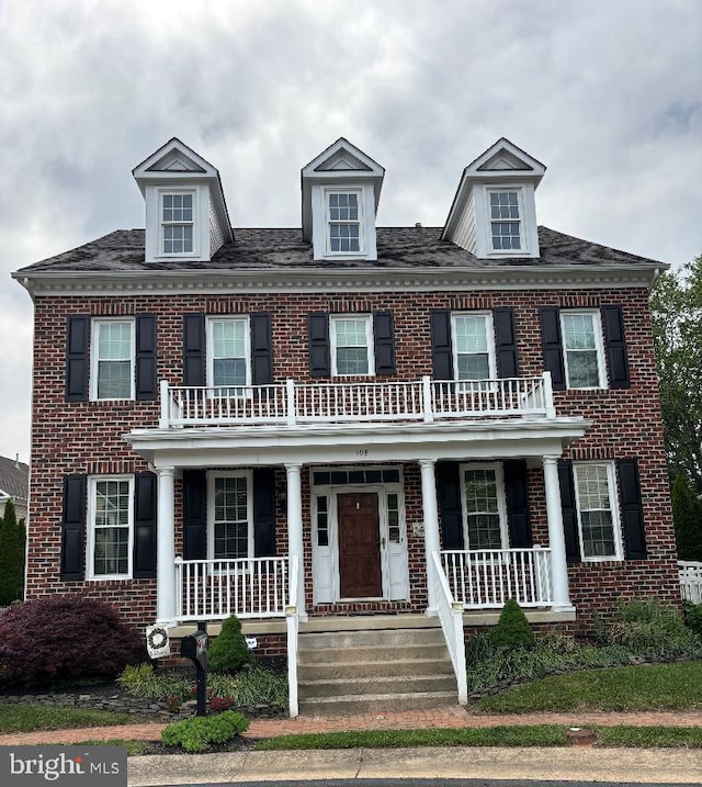 colonial-style house with covered porch, a balcony, and brick siding