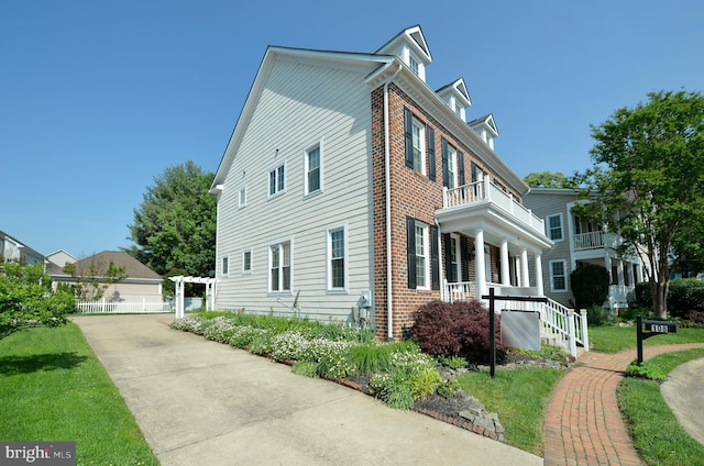 view of side of property featuring brick siding, a balcony, and a porch