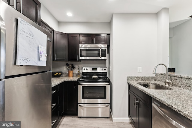 kitchen featuring stainless steel appliances, a sink, light stone counters, light wood-style floors, and recessed lighting
