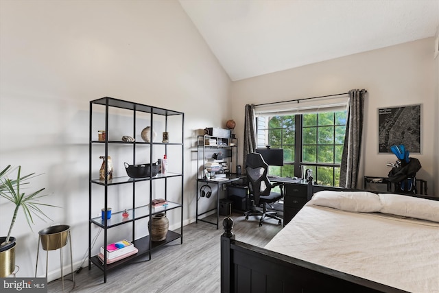 bedroom featuring a desk, light wood finished floors, and high vaulted ceiling