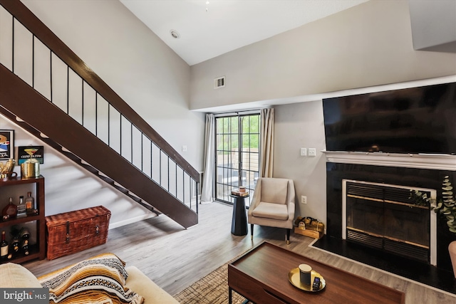 living area featuring wood finished floors, stairway, a towering ceiling, and a glass covered fireplace