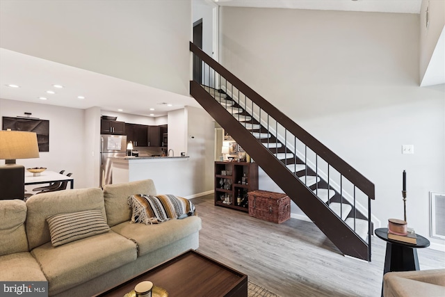 living area featuring light wood finished floors, stairs, recessed lighting, baseboards, and a high ceiling