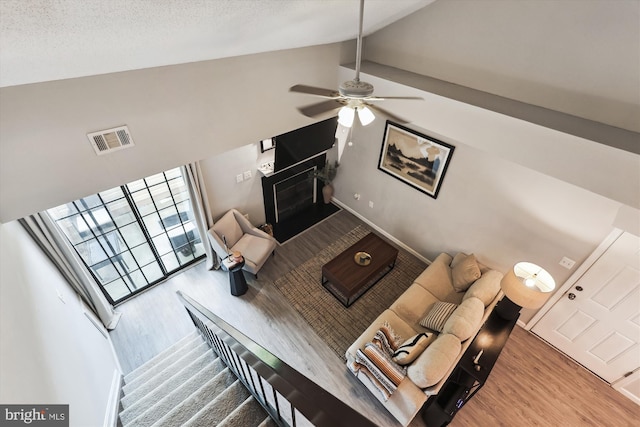 living area featuring wood finished floors, a ceiling fan, a fireplace, and high vaulted ceiling