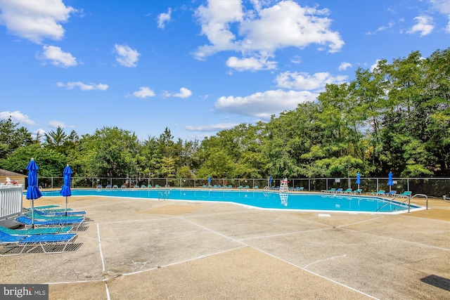 community pool featuring fence, a patio, and view of scattered trees