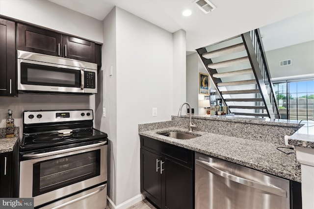 kitchen with stainless steel appliances, a sink, light stone countertops, and dark brown cabinetry