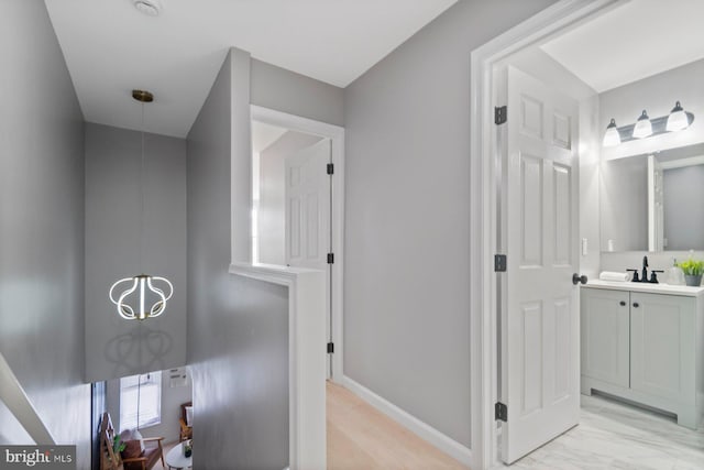 corridor with baseboards, light marble finish flooring, and a sink