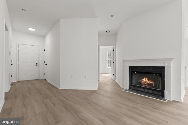 unfurnished living room featuring light wood finished floors, baseboards, a warm lit fireplace, and recessed lighting