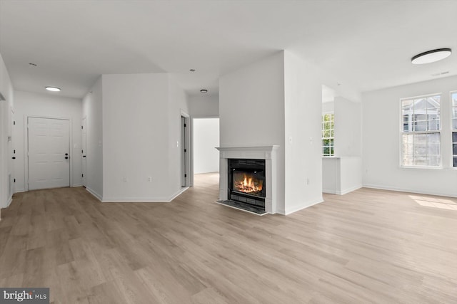 unfurnished living room featuring light wood-type flooring, a fireplace with flush hearth, and baseboards