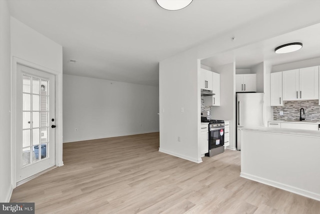 kitchen with stainless steel range with gas cooktop, freestanding refrigerator, open floor plan, under cabinet range hood, and backsplash